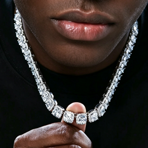 Close‑up portrait of black male model gently holding 10MM Glacier Cushion Clustered Tennis Chain in White Gold, showcasing hand‑set clustered halo cushion VVS simulated diamonds icy bling hip hop necklace, studio shot against solid dark black background highlighting stone sparkle and prong setting craftsmanship RDRIP JEWELRY