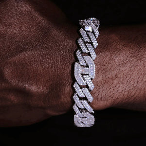 12mm Prong Set Iced Baguette Curb Bracelet White Gold Plated close up shot on dark skin man wrist, detailed view of hand prong set rectangular baguette VVS simulated diamonds on curb links, fully flooded icy bling thick mens curb wrist chain, full stone encrusted links and iced clasp, premium hip hop streetwear jewelry for men shiny reflective diamond curb bracelet RDRIP JEWELRY