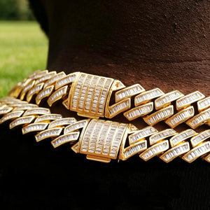 14MM Baguette Channel‑Set Miami Cuban Link Necklace macro close‑up shot,18K gold plated full iced‑out men hip hop chain,hand‑set flawless VVS simulated baguette stones,detailed view of fully encrusted box clasp lock,two stacked gold chains resting on deep dark skin neck,outdoor blurred green grass background,luxury heavy bling rapper streetwear jewelry RDRIP JEWELRY