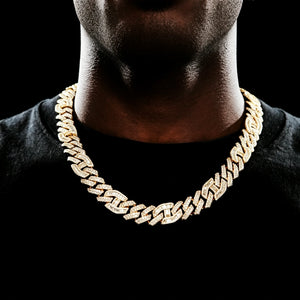 Close‑up neck shot of 15mm prong‑set mixed‑stone iced cuban curb chain worn by black man with very short stubble beard, wearing black crew neck shirt against dark black background, 18K gold plated pure copper men hip hop necklace, hand‑set baguette cut and round VVS simulated diamonds full iced‑out heavy streetwear bling jewelry RDRIP JEWELRY