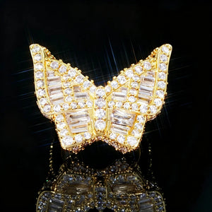 18K gold‑plated iced out baguette butterfly ring front close‑up shot, heavy 3D hip hop men statement ring, densely hand‑set baguette cut and round cubic zirconia rhinestone stones, brilliant sparkling bling diamond‑simulated jewelry, star‑burst light effect on black reflective studio background RDRIP JEWELRY