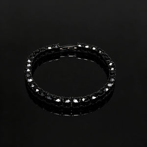 Slight angle view of 5mm Black Iced Out Tennis Bracelet, hand‑set flawless VVS black simulated diamonds, alloy material with vacuum black plating, single row hip hop bling tennis bracelet with secure box clasp, unisex dark streetwear wrist jewelry for men and women, product photograph on pure black glossy reflective surface, RDRIP JEWELRY