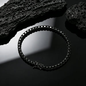 Top‑down overhead view of 5mm Black Iced Out Tennis Bracelet, hand‑set flawless VVS black simulated diamonds, alloy with vacuum black plating, single row hip hop bling bracelet with visible safety box clasp, styled with natural black volcanic rock accent on glossy pure black reflective surface, dark streetwear unisex wrist jewelry for men and women, RDRIP JEWELRY