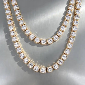 RDRIP 10MM Cushion Clustered Tennis Chain gold finish, product flat lay of two staggered‑size chains stacked on smooth border‑less grey reflective board. Cushion halo VVS simulated diamonds, thick gold plating, hip‑hop stacking statement jewelry for men and women RDRIP JEWELRY