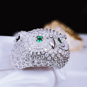 Extreme close‑up detail shot of white gold plated Iced Owl King Ring held by white soft glove, showcase intricate owl feather scale craftsmanship, bright emerald green eyes, densely set flawless VVS simulated diamonds, blurred gold ring in background, luxury iced out hip hop mens jewelry RDRIP JEWELRY