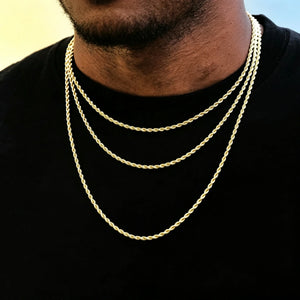 Extreme closeup portrait of Black male model with ultra short stubble beard wearing three different lengths 2mm 18k gold plated twisted rope layered necklaces, slim dainty twist link stackable chain for men hip hop streetwear, timeless minimalist unisex jewelry staple that can be worn solo or matched with custom pendants, anti-tarnish hand polished gold rope chain, soft smooth pale yellow and light blue gradient solid background, clean studio product photography for rap everyday accessories RDRIP JEWELRY