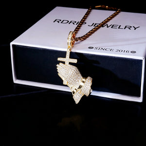 Gold plated iced out praying hands cross pendant hip hop necklace laid on official RDRIP JEWELRY gift box, flawless vvs simulated diamonds premium mens religious bling jewelry dark studio unboxing product shot RDRIP JEWELRY