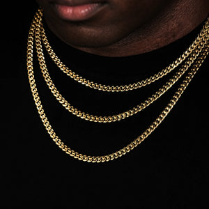 Extreme close-up shot focusing on male lips and neck area, Black male model with ultra-short trimmed stubble beard wearing three layered stackable 5mm Miami Cuban Link Chain in polished 18k gold plated finish, sleek glossy gold cuban link necklace for men hip hop streetwear, flexible tangle-resistant link structure, available lengths 18 inch, 20 inch, 24 inch, 30 inch with weight ranging from 24 grams to 38 grams and ±5 gram weight tolerance, fade-resistant anti-tarnish 18k gold plating, versatile layering