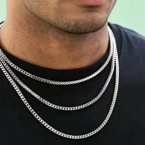 Neck closeup shot of Black male model with ultra-short trimmed stubble beard, wearing three layered stackable polished 3mm white gold Italian Franco link chain necklaces, flexible tangle-free Franco curb chain for men hip hop streetwear fashion, premium anti-tarnish stainless steel unisex minimalist layering jewelry, sleek thin hand-polished Franco chain available in 18 inch and 20 inch lengths, lightweight shiny everyday wearable statement necklace, can be worn solo or matched with custom hip hop pendants