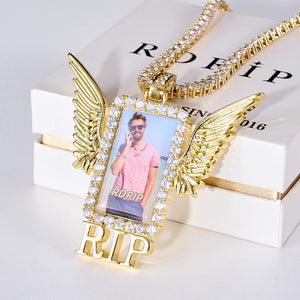 Iced Out Wings RIP Custom Photo Pendant, gold tone oblique front view, angel wing rectangular custom photo frame pendant with RIP letter decoration, encrusted round stones, matched tennis chain laid on official RDRIP branded gift box, light studio background, memorial personalized hip hop keepsake jewelry, RDRIP JEWELRY