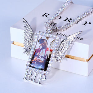 Iced Out Wings RIP Custom Photo Pendant, white gold tone oblique front view, angel wing rectangular custom photo frame pendant with RIP letter detail, encrusted round stones, matched tennis chain laid on official RDRIP branded gift box, light studio background, memorial personalized hip hop keepsake jewelry, RDRIP JEWELRY