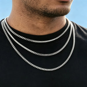 Close up model shot of men wearing three layered stackable 3mm polished white gold Italian Franco link chain necklaces, flexible tangle-free Franco curb chain for hip hop streetwear fashion, solid polished stainless steel unisex minimalist layering jewelry, sleek thin Franco chain available in 18 inch and 20 inch lengths, lightweight anti-tarnish everyday statement necklace perfect for solo wear or matching custom hip hop pendants, clean plain light blue background solid black tee, no dust or skin flake ble