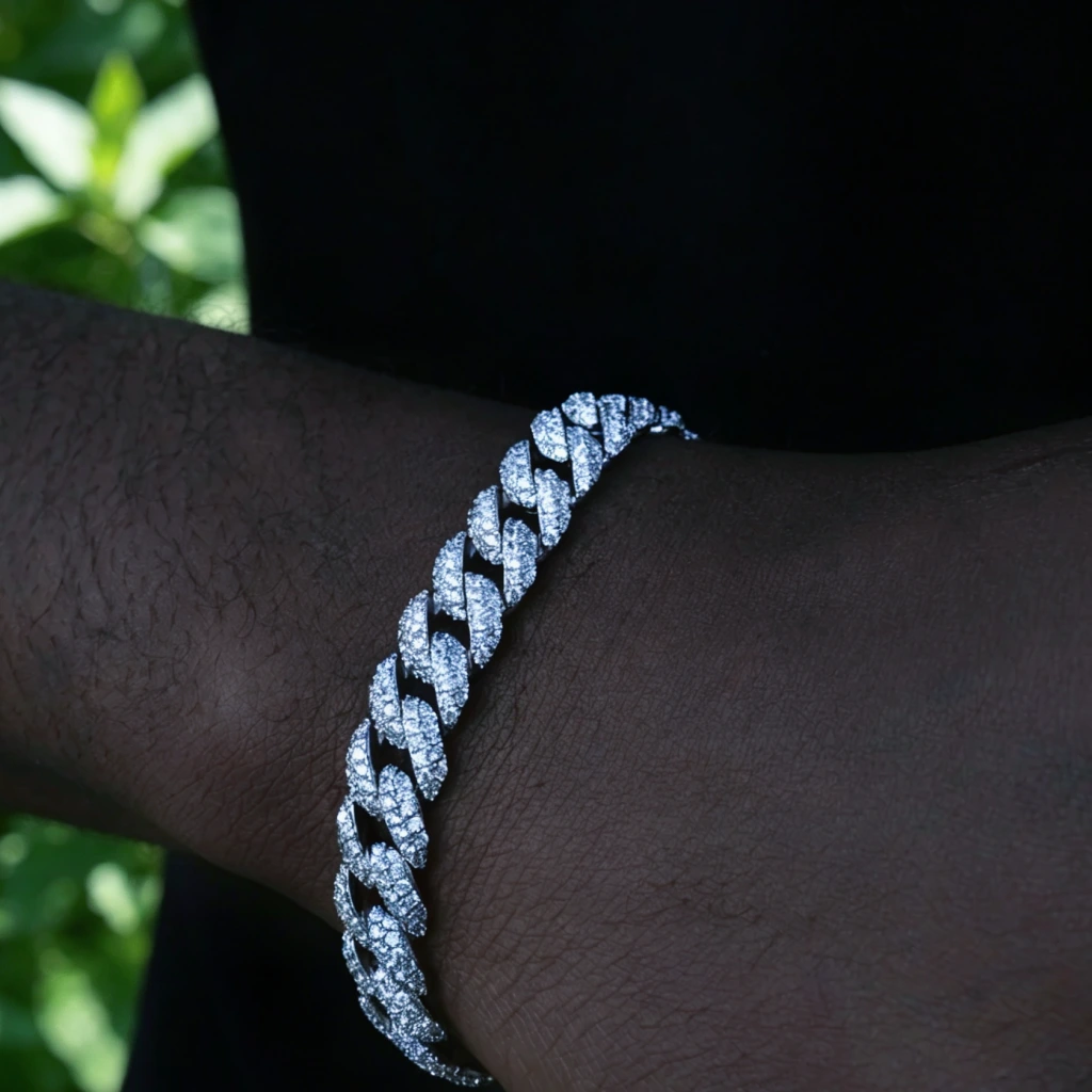 Side profile closeup of 10.5mm full iced out white gold plated miami cuban link bracelet worn on dark skin male wrist, custom molded copper hip hop wrist accessory with hand prong set flawless VVS simulated diamonds, dark toned studio shot with lush green leaf plant background, thick icy cuban bracelet for men streetwear rapper fashion, available in 7 inch 8 inch 9 inch sizes, heavy bling statement jewelry for hip hop enthusiasts, premium men's gift bracelet with lifetime warranty, RDRIP JEWELRY