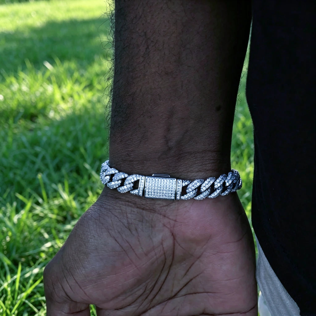 Close up shot of 10.5mm full iced out white gold plated cuban link bracelet with fully diamond covered box clasp worn on men's wrist, custom molded copper hip hop wrist jewelry with hand-set prong-lifted flawless VVS simulated diamonds, outdoor photo with fresh green grass background, heavy bling miami cuban bracelet for rappers streetwear fashion, available in 7 8 9 inch lengths, premium icy statement accessory for men hip hop gift, RDRIP JEWELRY