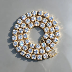 10MM Cushion Clustered Tennis Chain in Gold overhead top‑down circular coiled layout resting on seamless edge‑free grey reflective surface, natural sun lighting producing bright diamond starburst sparkles and light flares, fully iced encrusted box clasp visible, hand‑set cushion halo VVS simulated diamond links, thick gold‑plated hip‑hop icy bling unisex statement necklace, realistic premium jewelry product photography RDRIP JEWELRY

