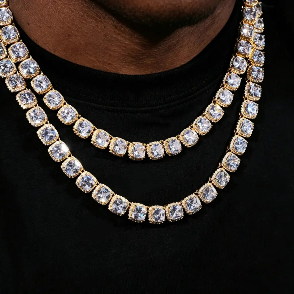 10MM Cushion Clustered Tennis Chain in Gold close‑up neck shot, layered stacked staggered‑length style on deep‑toned clean‑shaven male model wearing plain black crew neck t‑shirt. Hand‑set cushion halo VVS simulated diamond links, bright starburst sparkle and crystal reflections, thick gold‑plated icy hip‑hop bling necklace, men streetwear statement jewelry lifestyle close‑up photograph RDRIP JEWELRY
