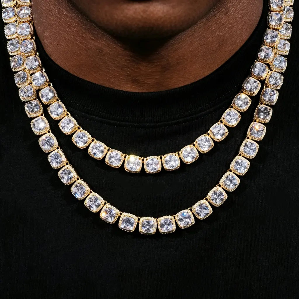 10MM Cushion Clustered Tennis Chain in Gold layered double‑stack wearing shot on deep skin clean‑shaven male model in plain black crew neck t‑shirt, two staggered length icy hip‑hop necklaces stacked together, hand‑set cushion halo VVS simulated diamond links, brilliant sparkling starburst stone reflections, thick gold‑plated unisex rap‑style statement jewelry lifestyle product photo RDRIP JEWELRY
