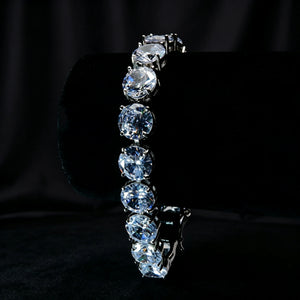 Vertical display of 10mm silver iced out sparkle tennis bracelet placed on black jewelry stand against solid seamless black backdrop, large round prong‑set VVS simulated diamond stones with brilliant sparkle, silver plated hip hop unisex bling wrist jewelry with heavy‑duty double lock safety clasp for men and women, RDRIP JEWELRY
