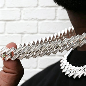14MM Baguette Channel‑Set Miami Cuban Link Necklace held in male hand, 18K white gold plated iced‑out hip hop chain, hand‑set flawless VVS simulated baguette stones, close‑up view of channel‑set cuban links and stone brilliance, blurred necklace on model in background, clean white brick wall backdrop, premium bling rapper streetwear jewelry RDRIP JEWELRY
