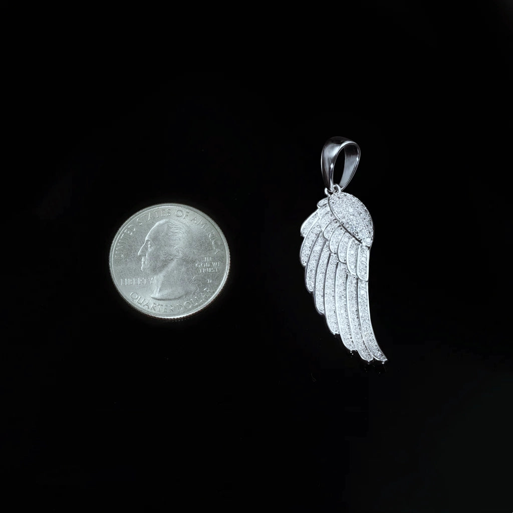 Size comparison view of 15mm Iced Micro‑Paved Single Seraph Wing Pendant in silver tone placed next to US quarter coin for scale reference, fully micro paved cubic zirconia feather wing charm against solid black background, RDRIP JEWELRY
