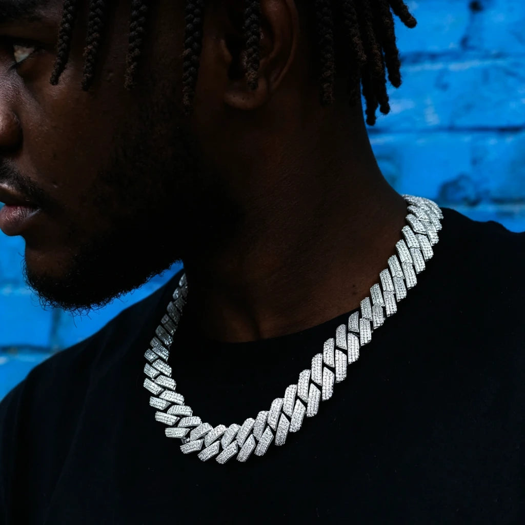 Men wearing 19mm full iced out prong set baguette cuban link chain necklace, thick wide hip hop bling cuban choker with fully paved rectangular VVS flawless simulated diamond stones, copper base 18k white gold finish, male model with short trimmed beard and long dreadlocks, shot against bright blue graffiti brick wall, trendy street hiphop men jewelry close up neck shot RDRIP JEWELRY
