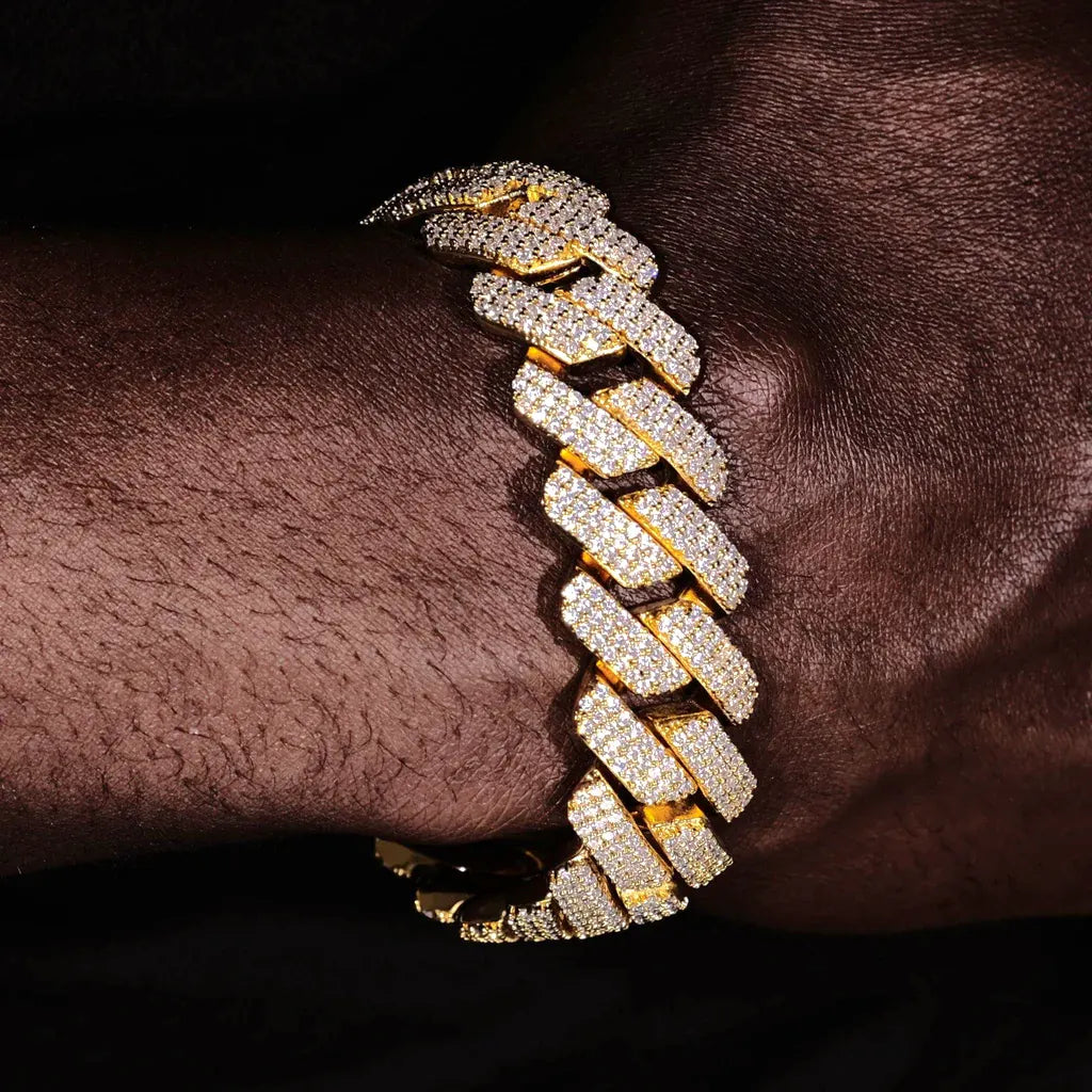Close-up wrist shot of a man wearing oversized 19mm Full Iced Out Prong Cuban Link Bracelet in shiny 18K gold plating, solid copper base fully encrusted with flawless lab-tested VVS simulated diamonds, brand new prong setting with completely iced clasp, heavy hip hop bling streetwear jewelry for men on dark skin tone against pure black background, luxury unisex diamond cuban bracelet RDRIP JEWELRY
