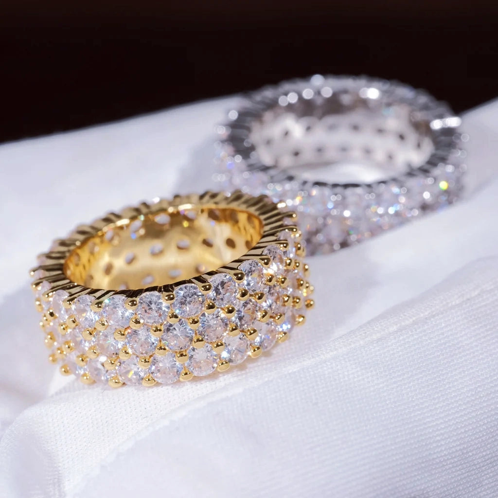 3‑Row Fully Paved Iced Out Eternity Ring gold plated ring in sharp foreground with blurred white gold plated ring on white cotton glove, 8mm width full wrap hip hop eternity band, hand‑set 4MM flawless VVS CZ simulated diamonds, heavy micro pave icy bling hip‑hop jewelry for men women, shallow depth of field studio product close‑up shot RDRIP JEWELRY SINCE 2016