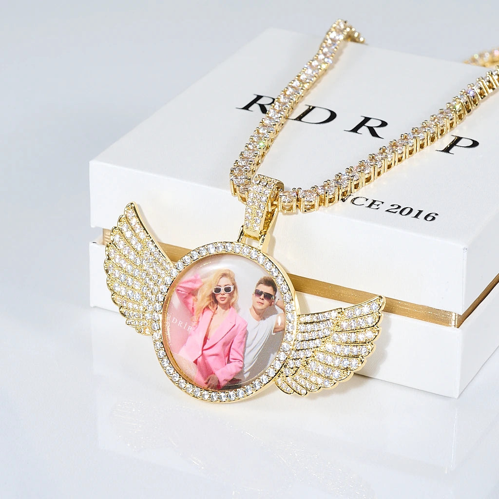 Gold 3D Angle Wing Custom Picture Pendant with iced tennis chain placed on RDRIP brand gift jewelry box, personalized custom photo hip hop jewelry product flat lay shot, RDRIP Jewelry
