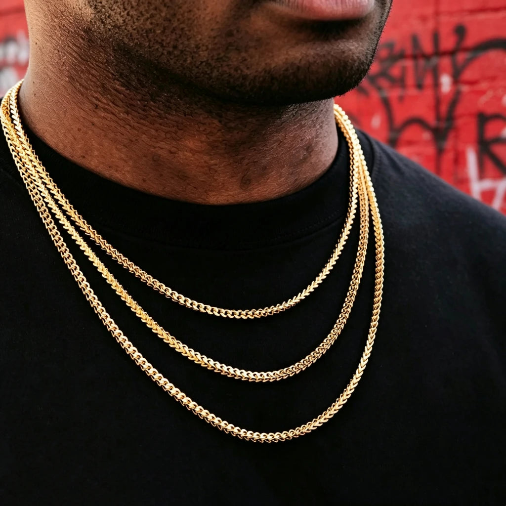 3mm 18k Gold Plated Franco Link Chain layered stacked necklace for men unisex hip hop streetwear jewelry, three different length Franco chains worn on black plain tee, dark skin male model shot against vibrant red graffiti wall background, polished shiny gold Italian design tangle resistant Franco link chain, classic layered hip hop bling necklace from RDRIP JEWELRY, perfect stacking gold chain pendant compatible everyday statement jewelry for street fashion lovers
