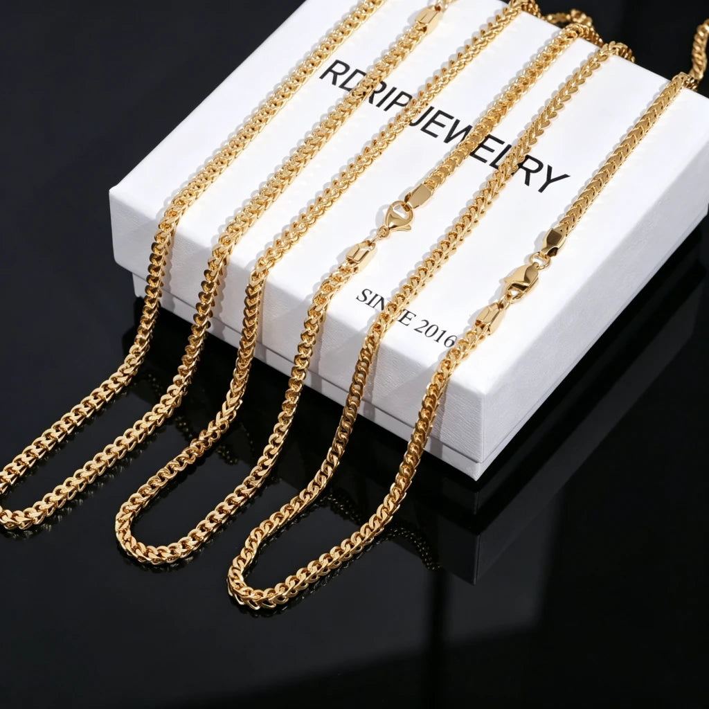 3mm 18k Gold Plated Italian Franco Link Chain multi size product display, multiple polished shiny gold Franco necklaces laid over branded white RDRIP JEWELRY jewelry box printed with SINCE 2016, smooth solid black reflective mirror background, flexible tangle resistant unisex hip hop stacking chain, available in 18 20 24 inch lengths, durable tarnish-free gold streetwear bling compatible with custom pendants, close-up studio product shot of classic layered statement necklace for men and women, premium hand-
