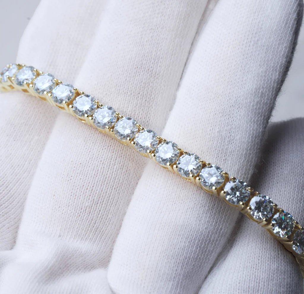 Bright studio close-up photograph of 4mm round brilliant cut D color VVS1 clarity moissanite tennis bracelet, solid S925 sterling silver base plated with thick 18K yellow gold, every clear moissanite stone securely hand prong set by skilled craftsmen, bracelet gently held by soft white cotton jewelry gloves on light neutral background, vivid rainbow sparkle and intense fire light reflecting from each flawless moissanite gemstone, unisex iced out hip hop luxury wrist chain for men and women, perfect for dail