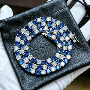 Coiled 4mm Iced Out Blue and White Alternating Tennis Chain, hand‑set VVS sapphire‑blue and white simulated diamond hip hop necklace resting on embossed RDRIP black leather jewelry pouch held in white cotton glove, unisex two‑tone bling tennis chain RDRIP JEWELRY
