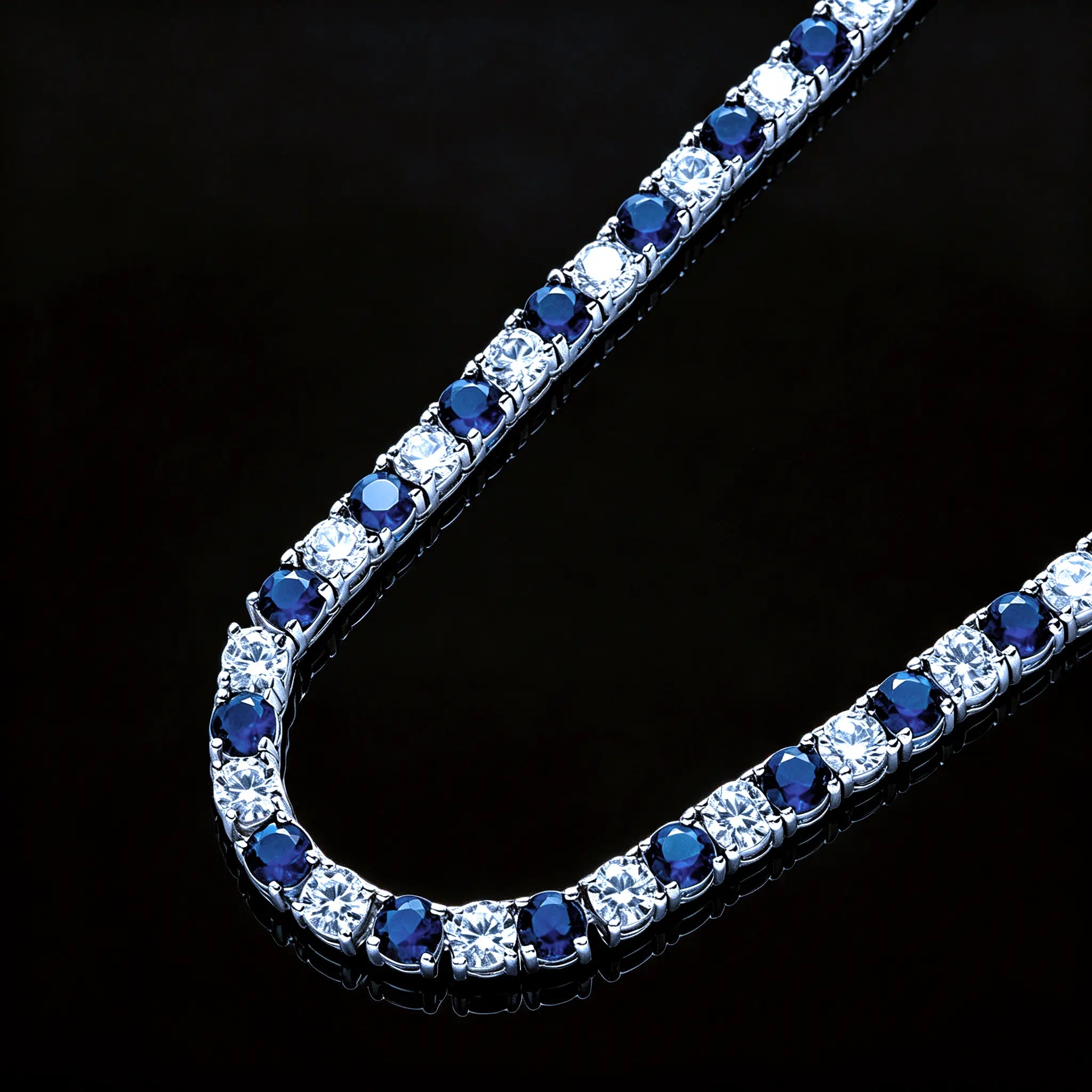 Macro close‑up shot of 4mm Iced Out Blue and White Alternating Tennis Chain, detailed view of hand‑prong‑set VVS sapphire‑blue and white round simulated diamonds, two‑tone hip hop bling necklace on pure black reflective display surface RDRIP JEWELRY
