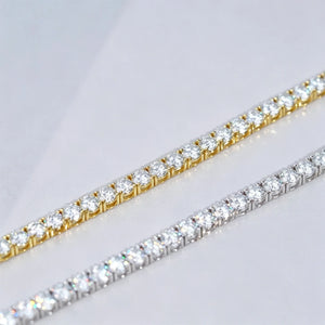 Side-by-side comparison macro shot of two 5mm D Color VVS1+ Hearts & Arrows cut moissanite tennis chains, one finished with thick 18K yellow gold plating and the other polished silver plating, both crafted on solid genuine S925 sterling silver base, every clear flawless moissanite stone precisely hand prong-set by professional jewelry artisans, striking rainbow light sparkle and bright crystal luster on each round gemstone, dual wrist chains laid parallel diagonally on smooth clean plain light grey