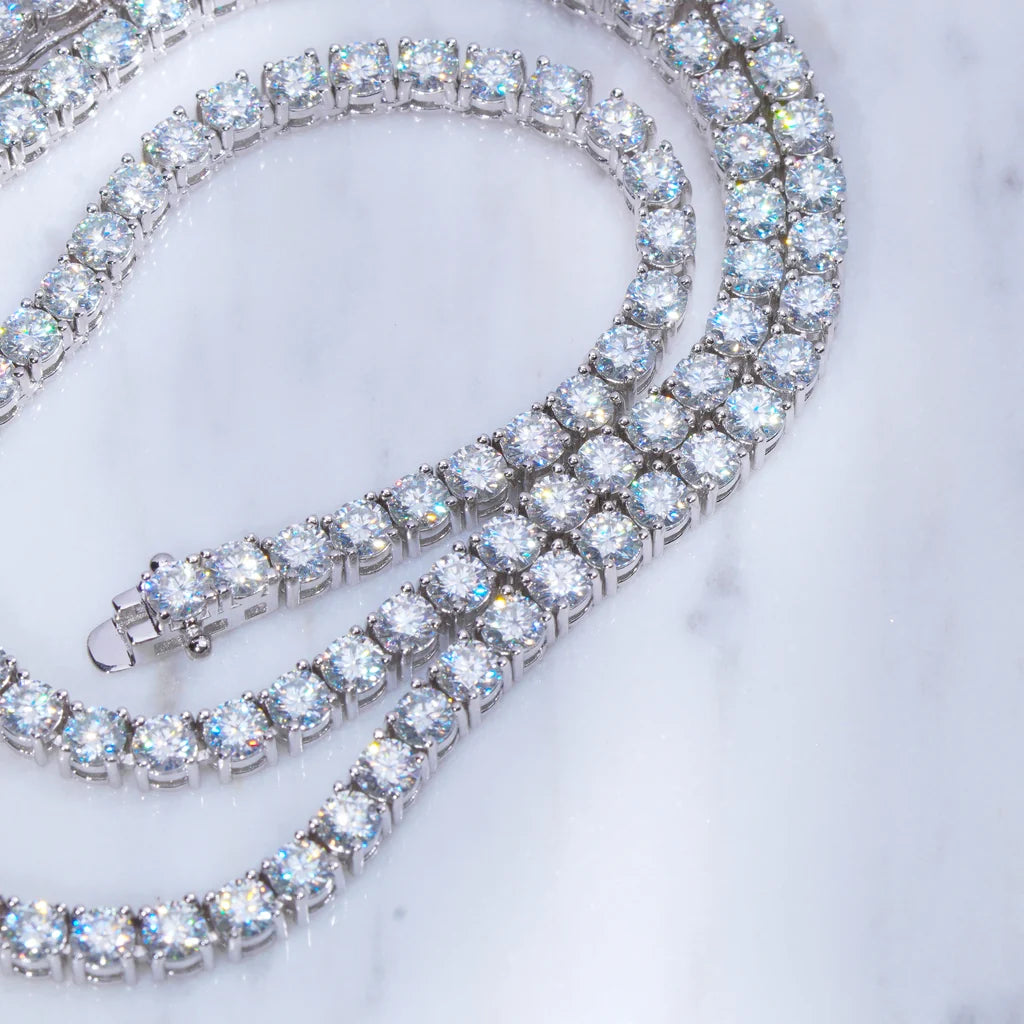 Full length flat lay shot of 5MM round VVS1 D color moissanite tennis chain necklace, solid S925 sterling silver with polished white gold plating, hand prong set clear moissanite stones with brilliant rainbow fire sparkle and sharp faceted shine, complete lobster lock clasp with safety side lock design, two coiled rows of icy bling tennis chain laid on clean light grey marble surface, smooth reflective silver metal setting, scratch-resistant anti-tarnish unisex hip hop iced out jewelry for men and women, pe