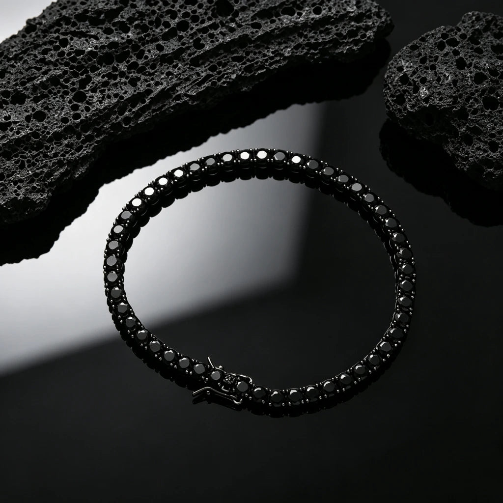 Top‑down overhead view of 5mm Black Iced Out Tennis Bracelet, hand‑set flawless VVS black simulated diamonds, alloy with vacuum black plating, single row hip hop bling bracelet with visible safety box clasp, styled with natural black volcanic rock accent on glossy pure black reflective surface, dark streetwear unisex wrist jewelry for men and women, RDRIP JEWELRY
