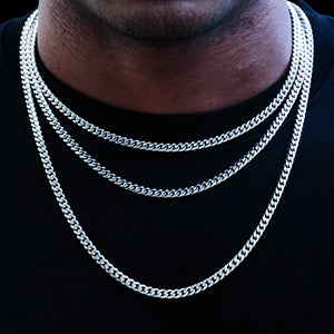 Studio shot with solid pure black background, black male model wearing layered stackable 5mm 18k white gold Miami Cuban link chain set, three multi-length cuban necklaces layered for hip hop streetwear styling, smooth fully polished tangle-free flexible uniform links, premium white gold plated anti-tarnish long-lasting shiny men’s urban statement jewelry, versatile design to wear alone or pair with custom hip hop pendants, expert hand-finished handcrafted artisan cuban chain, suitable for daily casual