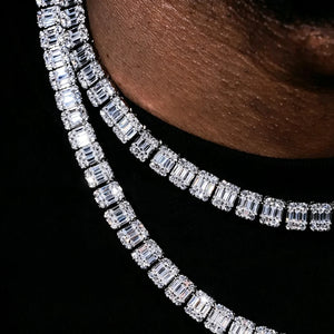 Macro detail close‑up shot of 8mm Iced Baguette Cluster Tennis Chain double layering necklace on lightly toned dark skin male model in black shirt, showcasing hand‑set mixed baguette and round VVS simulated CZ stones, sparkling iced‑out hip‑hop unisex jewelry, dark deep‑blue studio backdrop RDRIP JEWELRY
