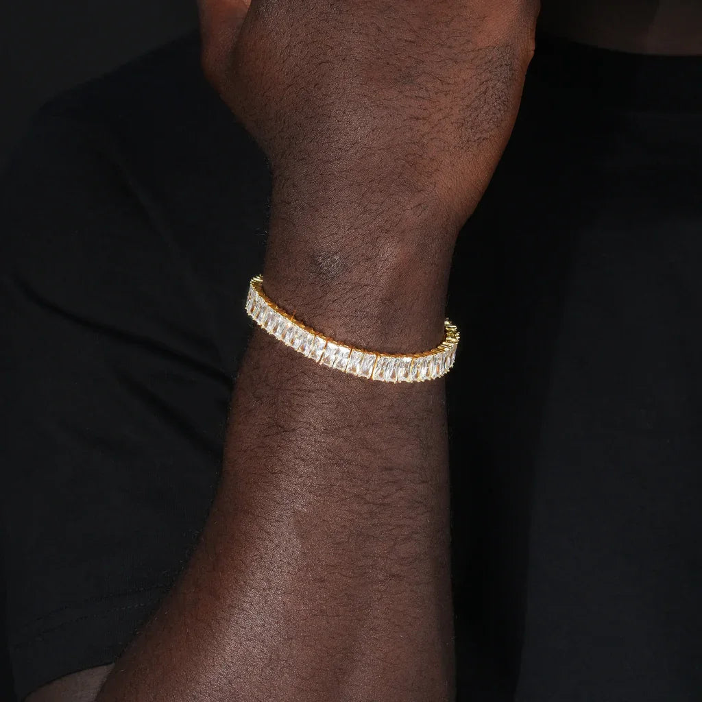 Blaze Retro Baguette‑Cut Iced Tennis Bracelet 18k gold plated worn on dark‑toned male wrist, men old‑school 90s hip‑hop bracelet, full row baguette‑cut AAA cubic zirconia stones, unisex iced‑out single row tennis chain bracelet, streetwear party hip‑hop outfit men’s statement jewelry RDRIP JEWELRY
