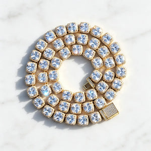 Top‑down coiled flat lay product photo of 10MM Glacier Cushion Clustered Tennis Chain in 18K Gold, featuring fully iced paved decorative clasp, flawless VVS cushion‑cut simulated cluster diamonds with bright sparkling light reflections, hand prong‑set hip hop bling necklace arranged in circular coil on clean subtle textured pure white marble surface, luxury unisex statement streetwear jewelry RDRIP JEWELRY
