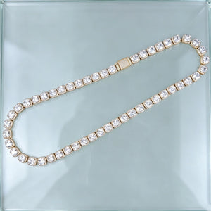 Top‑down flat lay product photograph showing full length of 10MM Glacier Cushion Clustered Tennis Chain in 18K Gold, complete iced‑out hip hop tennis necklace with fully paved diamond lock clasp, hand‑set flawless VVS cushion cut simulated cluster diamonds with bright sparkling reflections, laid flat on seamless clear transparent glass surface, luxury unisex streetwear bling statement jewelry RDRIP JEWELRY
