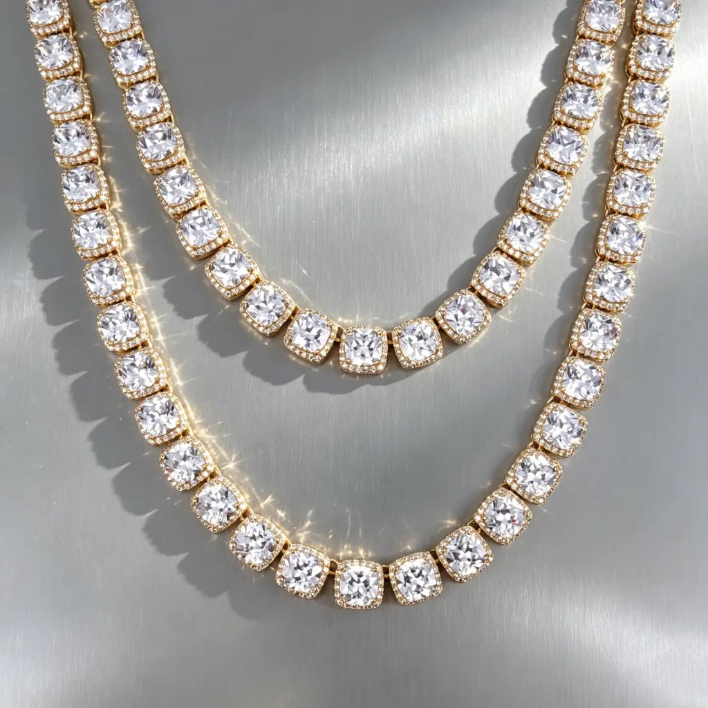 RDRIP 10MM Cushion Clustered Tennis Chain gold finish, product flat lay of two staggered‑size chains stacked on smooth border‑less grey reflective board. Cushion halo VVS simulated diamonds, thick gold plating, hip‑hop stacking statement jewelry for men and women RDRIP JEWELRY