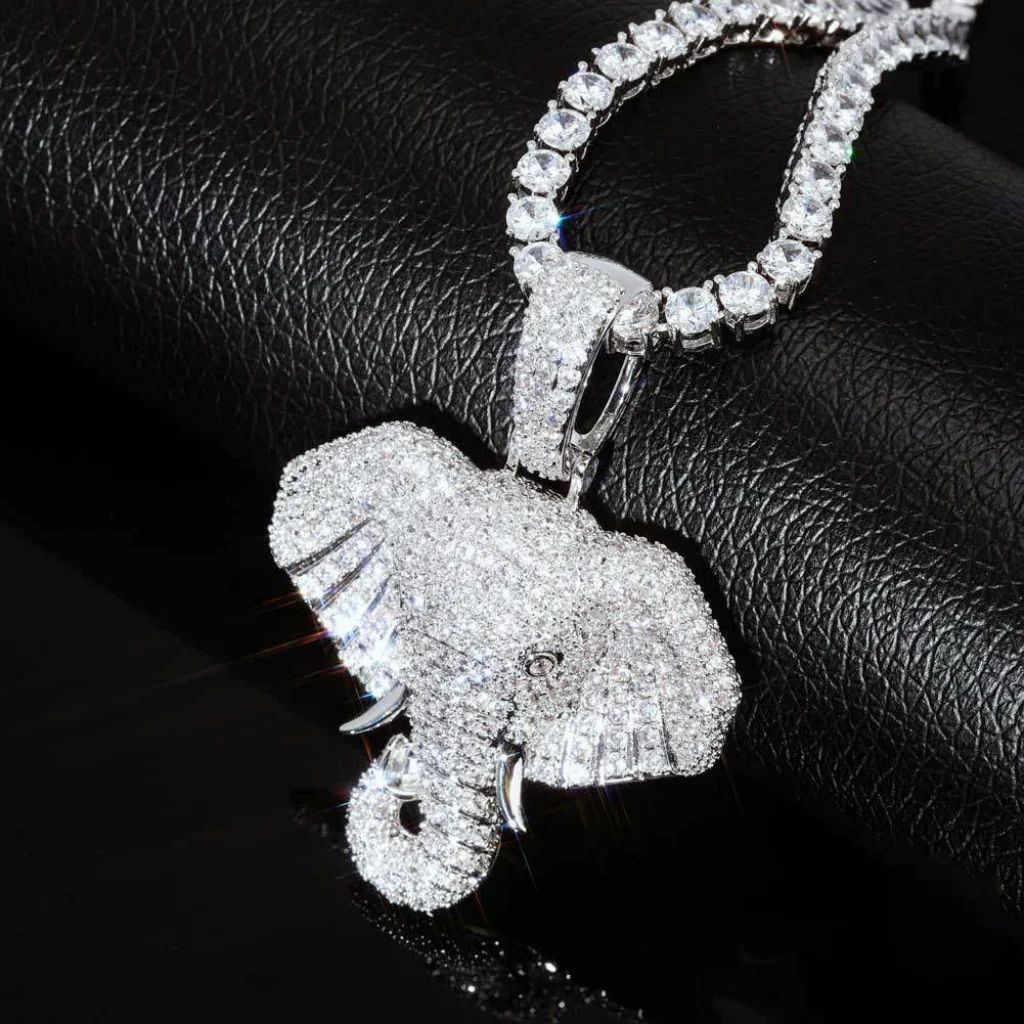 Extreme close‑up shot of iced micro paved pharaoh elephant head pendant, silver finish fully set with AAA cubic zirconia stones, paired with sparkling tennis chain, brilliant stone sparkle on textured black leather surface, premium hip hop bling charm for men RDRIP JEWELRY
