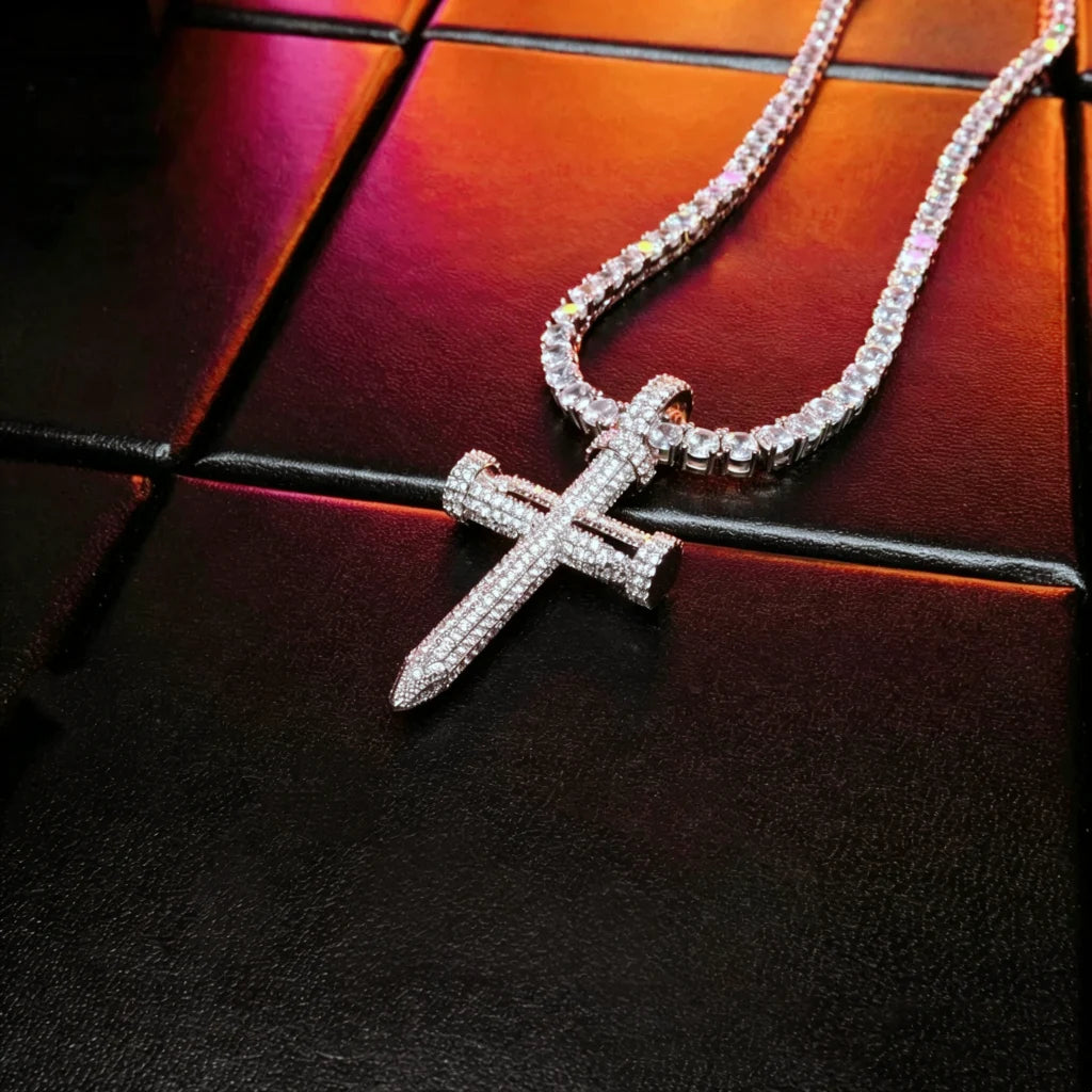 Flat lay shot Iced Out Nail Cross Pendant full pave AAA cubic zirconia silver tone nail shaped crucifix men necklace, bling iced‑out hip hop jewelry set with tennis chain laid on textured black leather surface RDRIP JEWELRY
