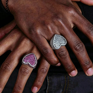 Model wearing iced out pave love heart couple ring set on dark skin hands, magenta pink and icy blue‑grey full micro paved heart rings, hand‑set AAA cubic zirconia stones, thick wide band unisex hip hop bling matching lover jewelry, real‑life wear showcase street fashion hip‑hop statement rings for men women RDRIP JEWELRY
