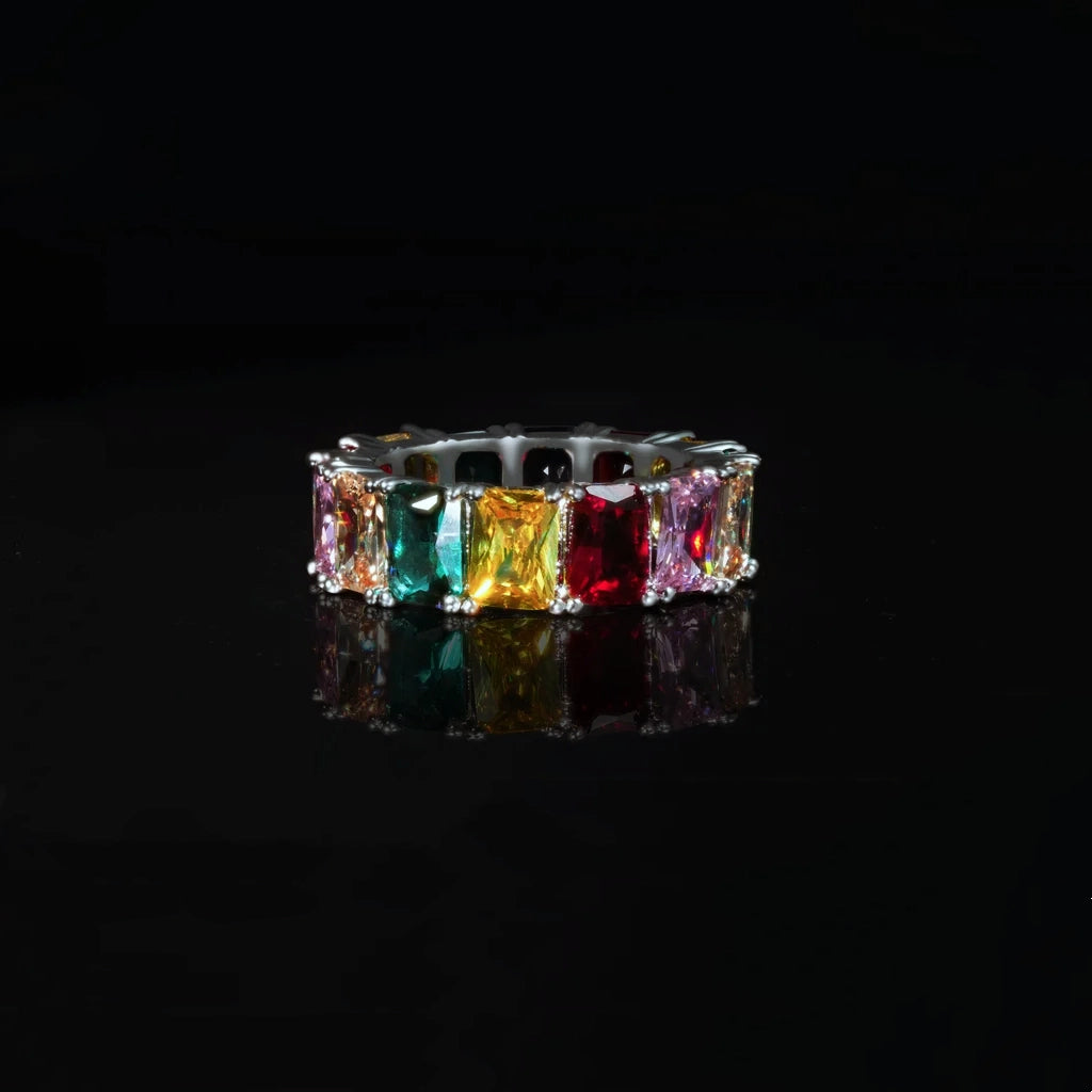 RDRIP JEWELRY Iced Out Rainbow Baguette Eternity Ring front view close up shot silver tone full band hip hop ring vivid multicolor baguette cut cubic zirconia stones on black glossy reflective background showcasing stone color and prong setting detail unisex bling statement jewelry

