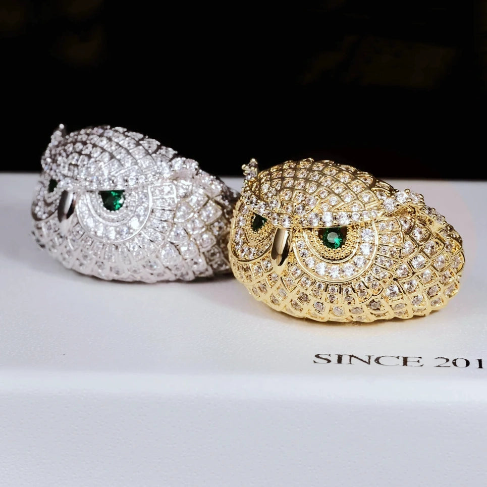 Angled product shot of Iced Owl King Ring, gold plated and white gold plated owl rings laying side by side, detailed scale texture, brilliant emerald green eyes, fully micro paved flawless VVS simulated diamonds, heavy hip hop mens statement bling jewelry RDRIP JEWELRY
