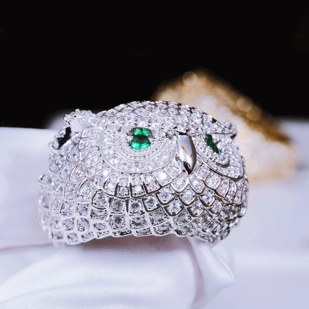 Extreme close‑up detail shot of white gold plated Iced Owl King Ring held by white soft glove, showcase intricate owl feather scale craftsmanship, bright emerald green eyes, densely set flawless VVS simulated diamonds, blurred gold ring in background, luxury iced out hip hop mens jewelry RDRIP JEWELRY
