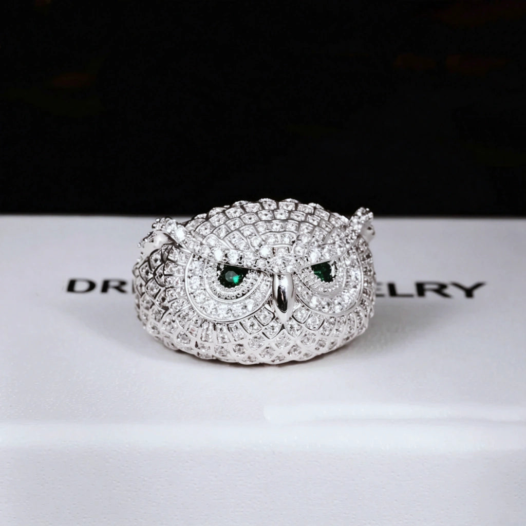 Close‑up studio photo of single white gold plated Iced Owl King Ring, detailed owl scale texture, vivid emerald green eyes, fully micro‑paved flawless VVS simulated diamonds, heavy weight iced out hip hop mens ring displayed on RDRIP JEWELRY branded box RDRIP JEWELRY
