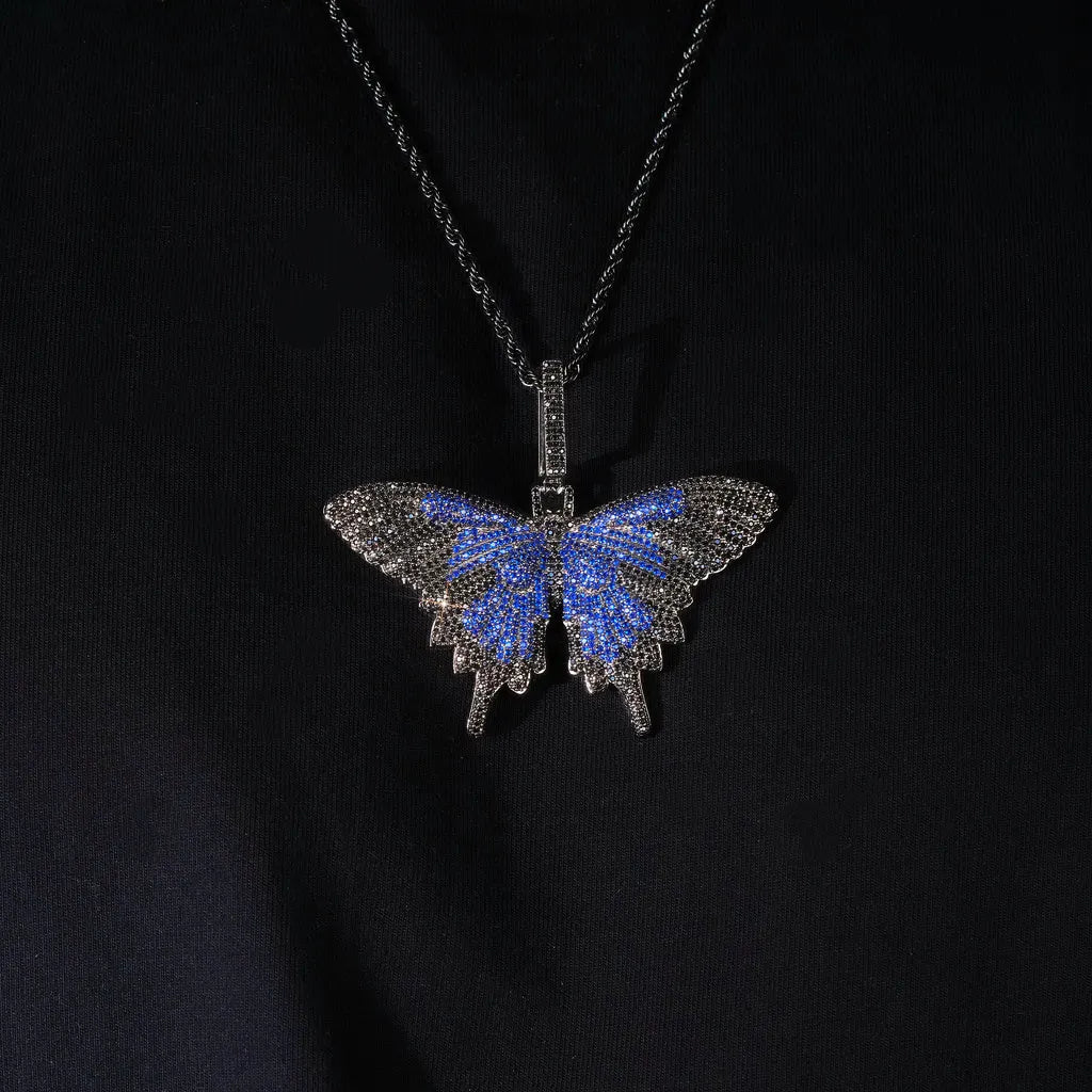 Micro‑pave iced out blue black butterfly pendant necklace black gunmetal tone paired with black twisted rope chain high angle flat lay studio shot full paved VVS simulated diamonds hip hop bling pendant on black fabric background RDRIP JEWELRY
